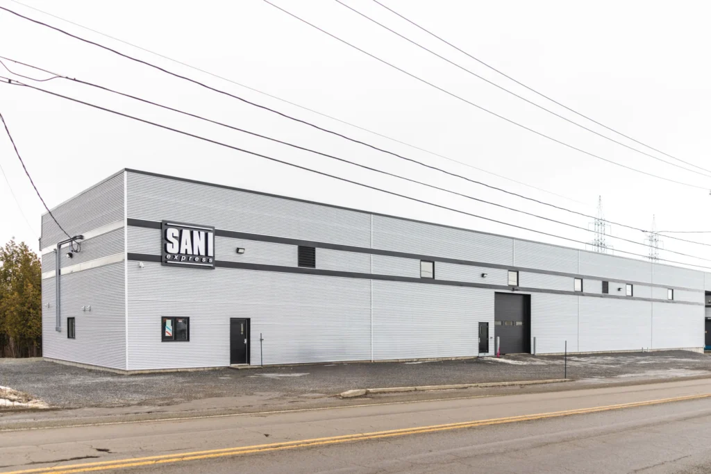 Bâtiment industriel SANI Express, solutions écologiques d'emballages et entretien, rue calme, arbres, lignes électriques.